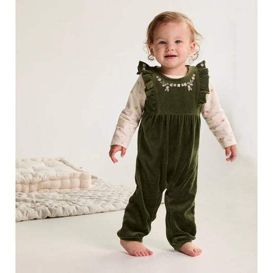 Child wearing a green velvet romper with floral embroidery on a white background