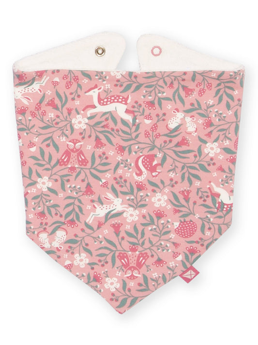 A triangular baby bib with a pink forest pattern featuring deer, foxes, owls, berries, and leaves, with a white fabric lining and snap closures at the top.