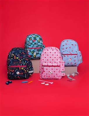 Four colorful patterned backpacks arranged on a bright red studio background, with small accessories placed in front. The backpacks include dark navy with multicolor graphics, teal with cartoon patches, pink with red hearts, and light blue with small pink motifs.